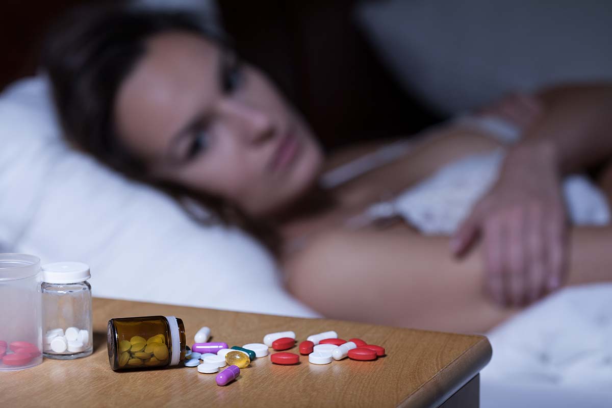 woman in bed looking at the pile of pills on her nightstand realizing she needs sleeping pills detox in fl