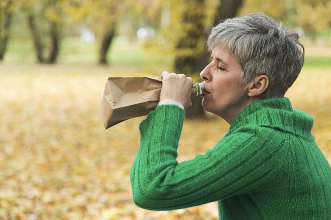 elderly woman in the park drinking alcohol in a paper bag showing elder substance abuse