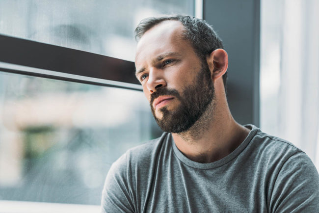 man looking out window while going through detox from methadone