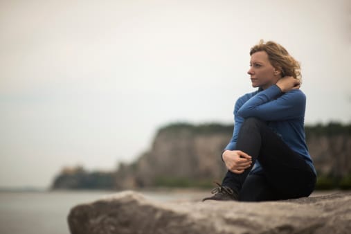 Woman on rock at beach deciding on inpatient vs outpatient rehab for her addiction.