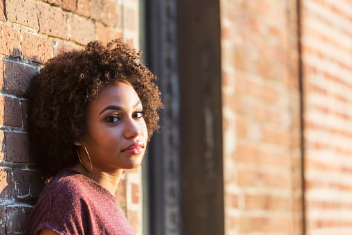 Woman leaning against wall wondering where the best addiction treatment programs are located.