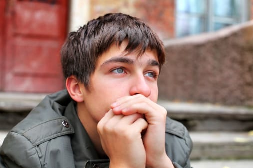 Sad young man on stoop worried about family codependency and trying to quit drugs.