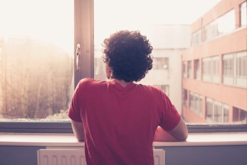 Person with back to camera looking out window knowing he or she has a marijuana addiction.