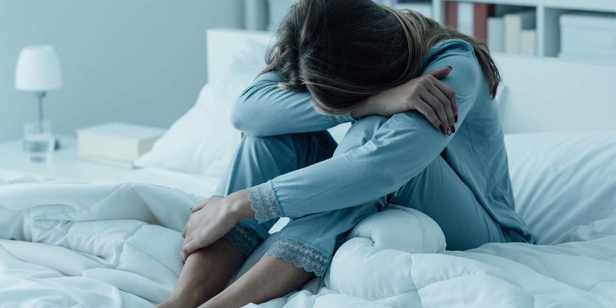 woman with her head on her knees in bed suffering from depression and substance abuse