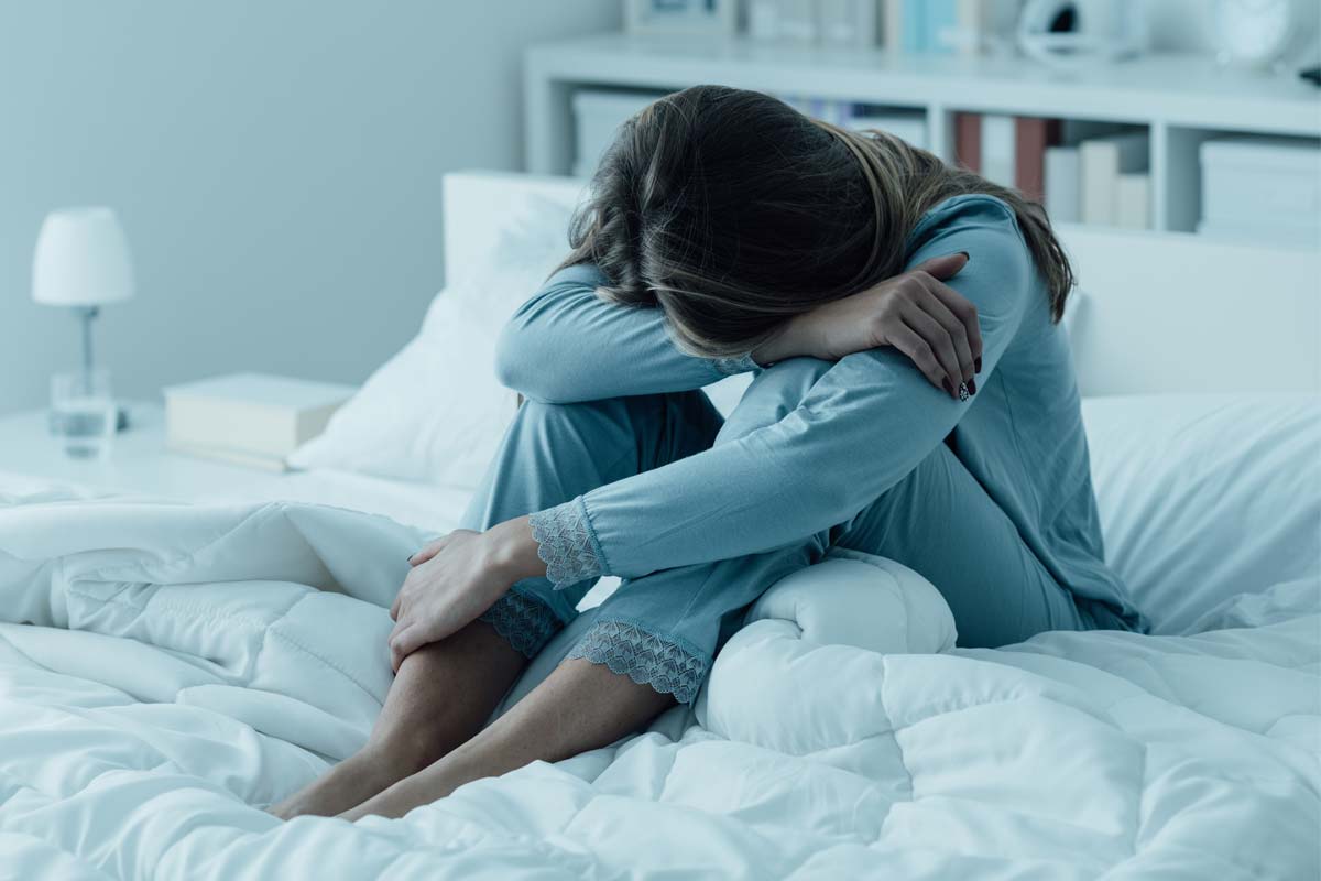 woman with her head on her knees in bed suffering from depression and substance abuse
