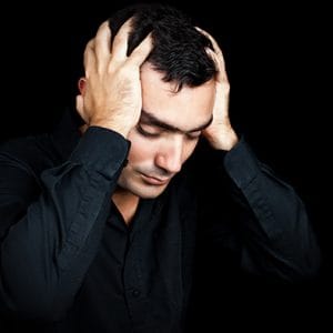 Man in black background with hands to head suffering a methadone addiction.