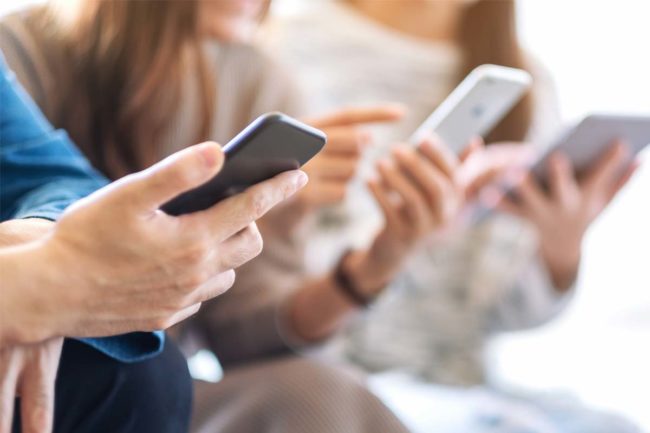 close up of friends sitting next to each other with a digital addiction while they stare at their phones