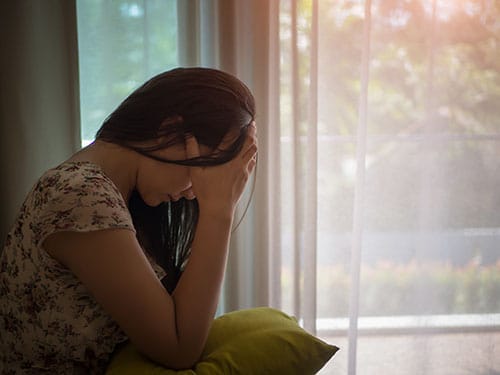 Crying woman next to window suffering with Xanax withdrawal.