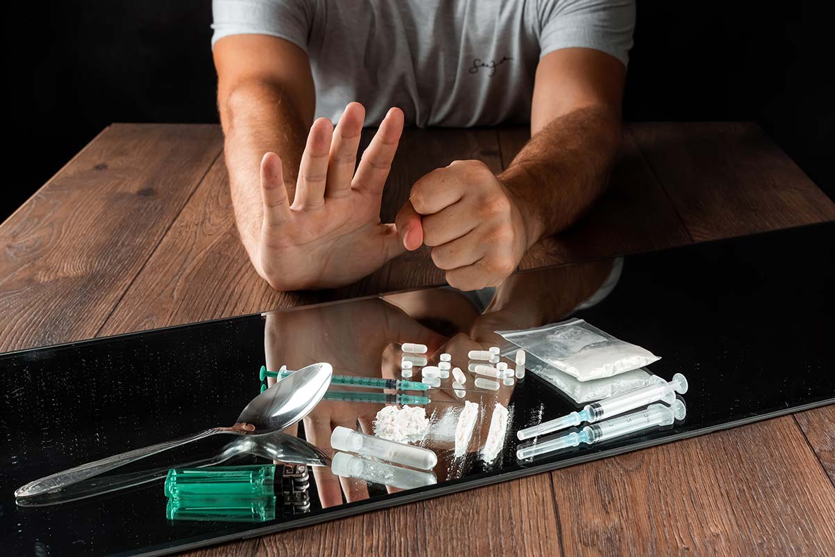 man putting a hand up and fist down in front of various drugs as he starts quitting drugs