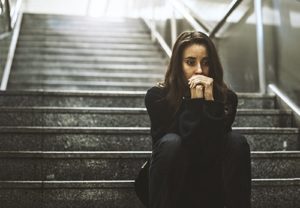 Sad young woman on dark steps suffering with depression from abuse of drugs