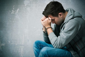 Depressed young man in dark place wondering is is schizophrenia vs psychosis or addiction
