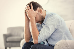 Man on sofa with hands on head showing signs of methadone abuse